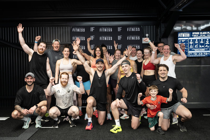 A diverse group of people at Inclusive Fitness celebrating together with raised hands